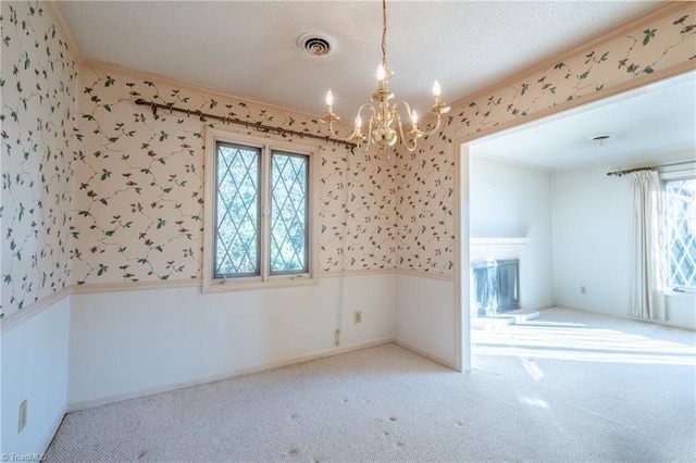 unfurnished room featuring visible vents, a notable chandelier, ornamental molding, carpet flooring, and wallpapered walls