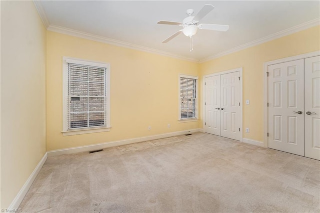 unfurnished bedroom with multiple closets, crown molding, light colored carpet, and ceiling fan