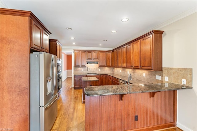 kitchen featuring a breakfast bar, appliances with stainless steel finishes, dark stone countertops, light hardwood / wood-style floors, and kitchen peninsula