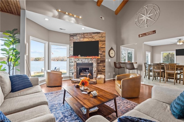 living room with ceiling fan, beamed ceiling, a stone fireplace, and hardwood / wood-style floors