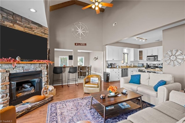 living room with light hardwood / wood-style floors, ceiling fan, a high ceiling, and a stone fireplace