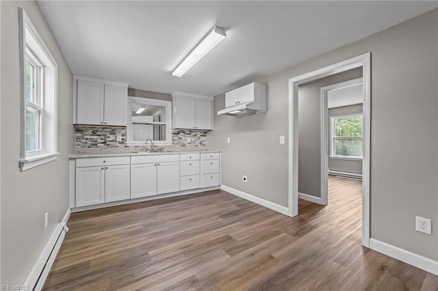 kitchen with baseboards, light countertops, a baseboard heating unit, white cabinets, and tasteful backsplash