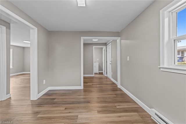 hall featuring baseboards, a baseboard radiator, wood finished floors, and a healthy amount of sunlight
