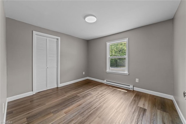 unfurnished bedroom featuring wood finished floors, baseboards, baseboard heating, and a closet