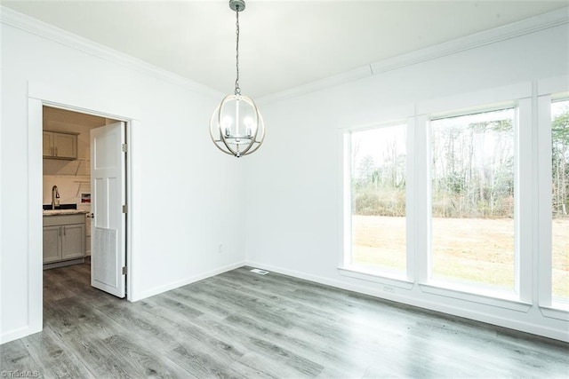 unfurnished dining area with light wood-style flooring, a sink, baseboards, an inviting chandelier, and ornamental molding