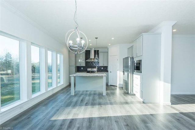 kitchen featuring an inviting chandelier, wall chimney range hood, a wealth of natural light, crown molding, and appliances with stainless steel finishes