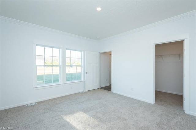 unfurnished bedroom featuring a walk in closet, baseboards, ornamental molding, and carpet flooring