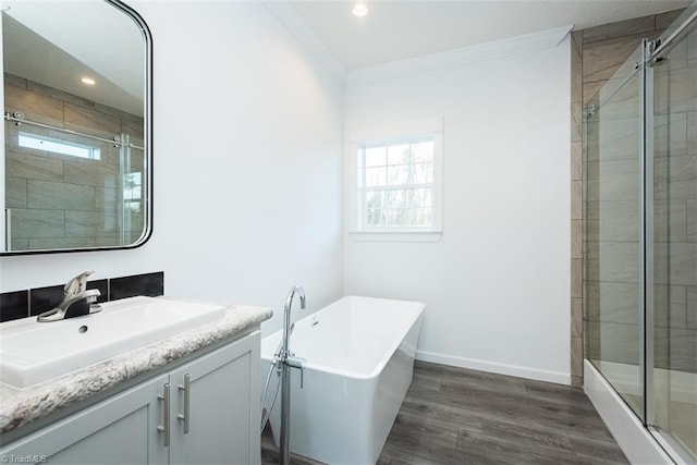 full bathroom with a shower stall, wood finished floors, vanity, ornamental molding, and a freestanding tub