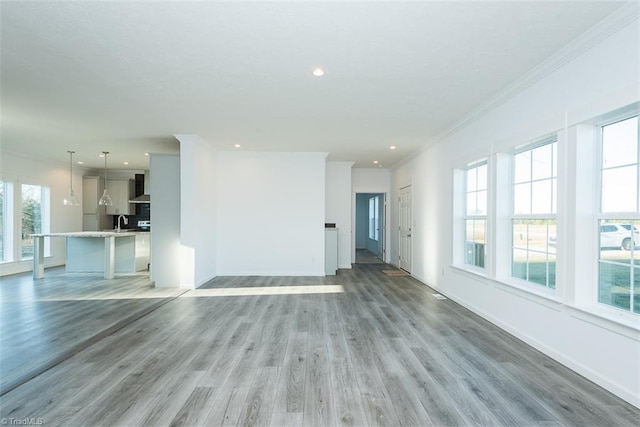 unfurnished living room with plenty of natural light, light wood-style flooring, and ornamental molding