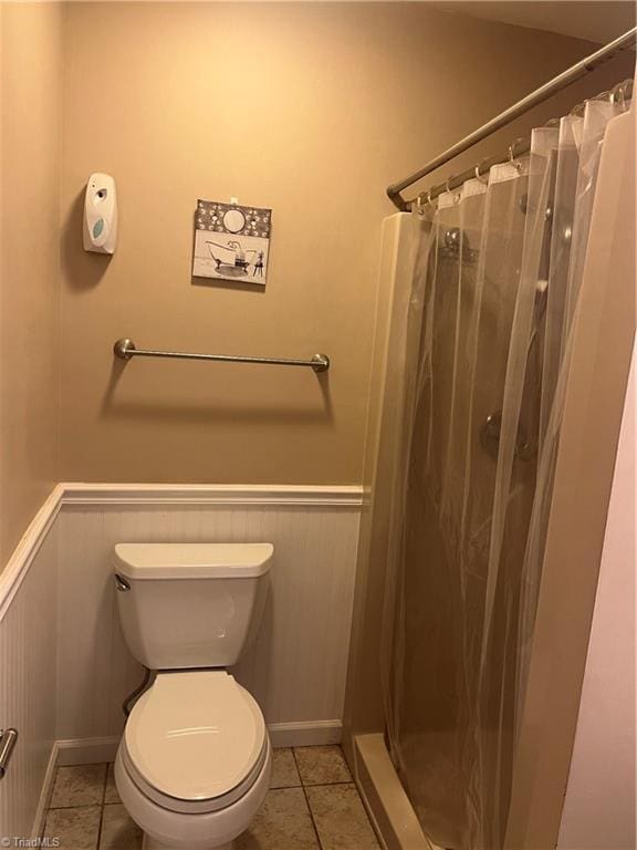 bathroom with toilet, a shower with shower curtain, wainscoting, tile patterned floors, and baseboards