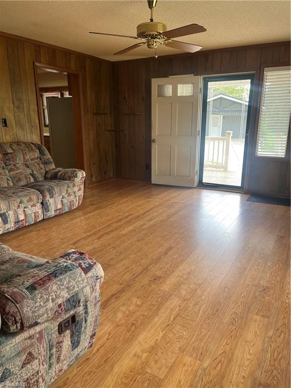 living room with wood walls, light wood-type flooring, a ceiling fan, and a textured ceiling
