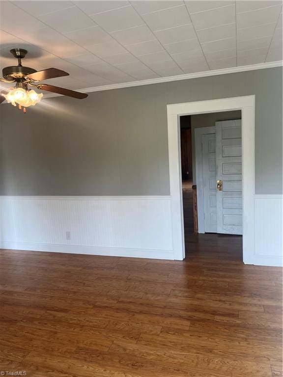 unfurnished room featuring dark wood finished floors, ornamental molding, a ceiling fan, and a wainscoted wall