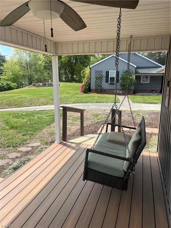 wooden terrace featuring ceiling fan and a lawn