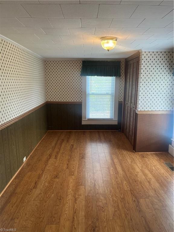 spare room with wallpapered walls, wood finished floors, wainscoting, and visible vents