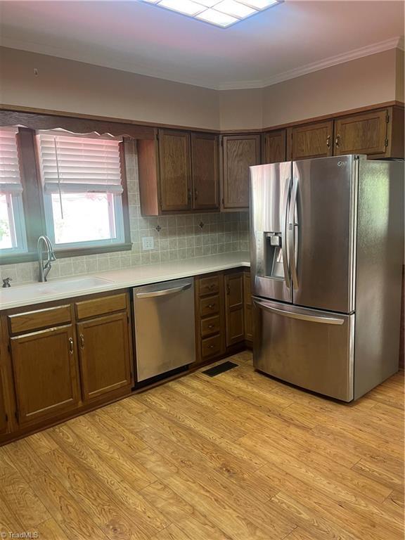 kitchen with stainless steel appliances, light countertops, a sink, and crown molding
