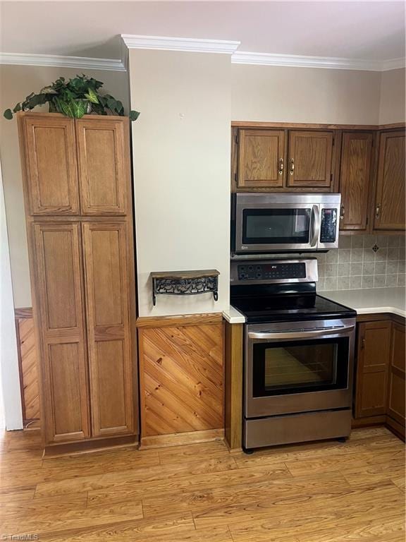 kitchen with light countertops, backsplash, crown molding, stainless steel appliances, and light wood finished floors
