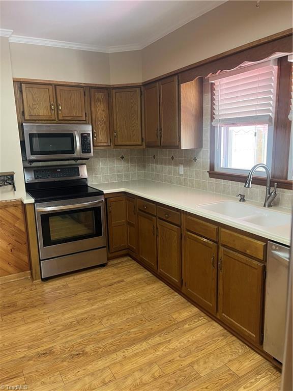 kitchen with tasteful backsplash, ornamental molding, appliances with stainless steel finishes, light countertops, and a sink