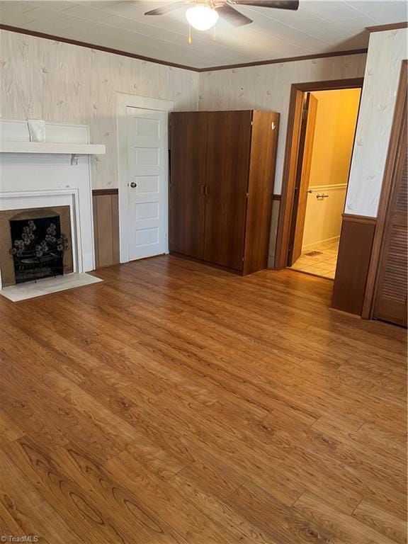 unfurnished living room featuring wooden walls, a ceiling fan, crown molding, and wood finished floors
