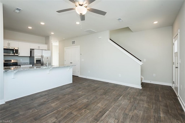 kitchen featuring appliances with stainless steel finishes, white cabinetry, a breakfast bar area, light stone countertops, and dark wood-type flooring