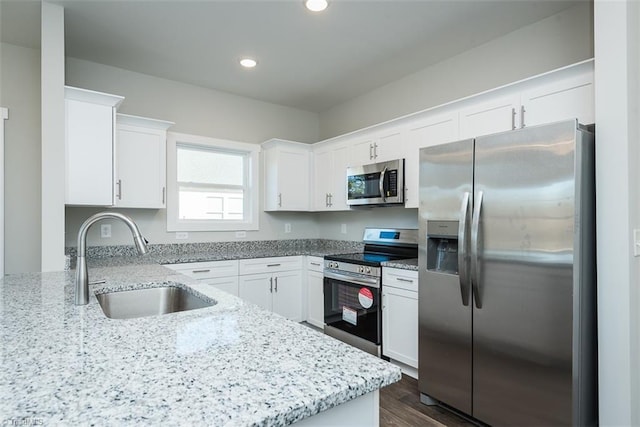 kitchen with appliances with stainless steel finishes, white cabinetry, sink, dark hardwood / wood-style flooring, and light stone countertops