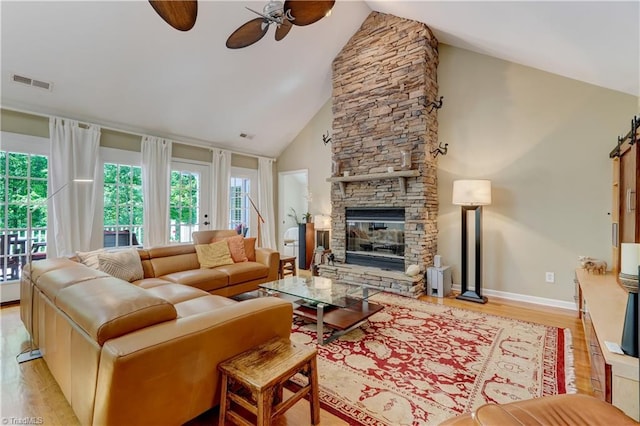 living room featuring visible vents, wood finished floors, baseboards, a stone fireplace, and ceiling fan