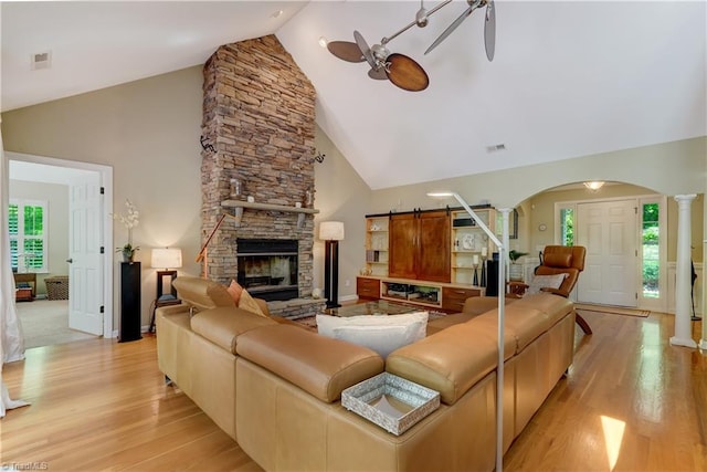 living area with arched walkways, light wood-style flooring, ceiling fan, and high vaulted ceiling