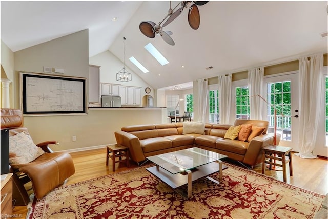 living room featuring ceiling fan, a skylight, high vaulted ceiling, baseboards, and light wood-style flooring