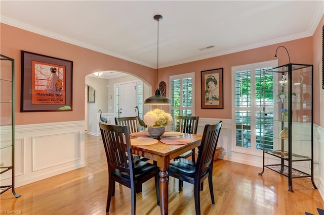 dining space featuring arched walkways, a wainscoted wall, light wood finished floors, and visible vents