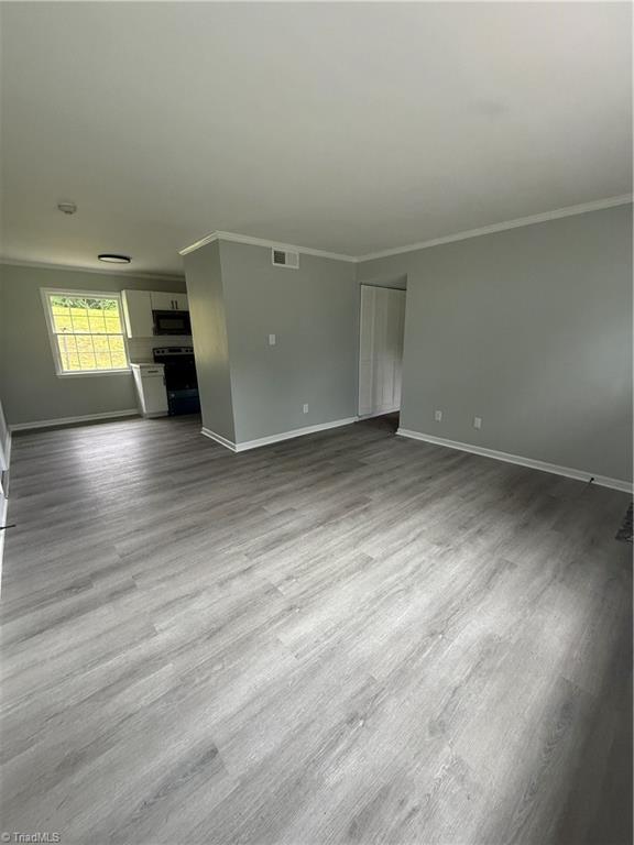 unfurnished living room featuring visible vents, ornamental molding, baseboards, and dark wood-style flooring