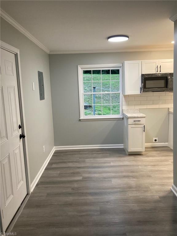 unfurnished dining area featuring baseboards, ornamental molding, and dark wood-style flooring
