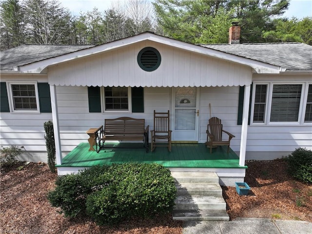 view of front of home with a porch, a chimney, and roof with shingles