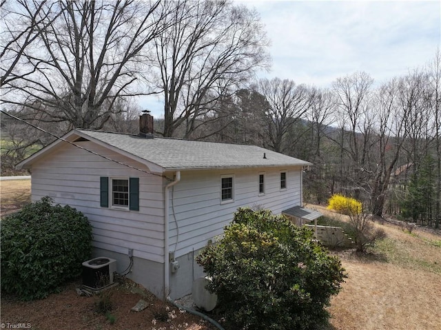 view of side of property featuring central air condition unit, roof with shingles, and a chimney