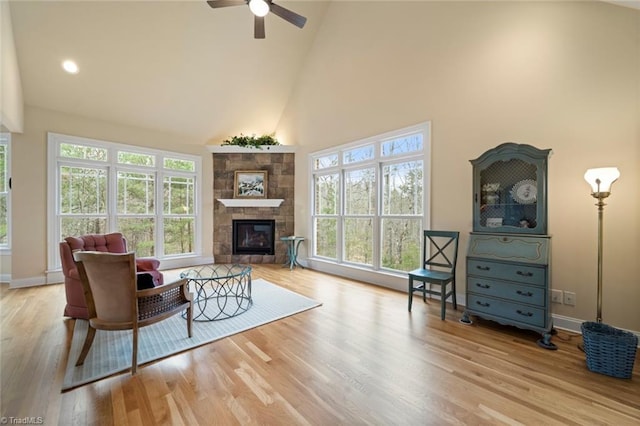 living room featuring a stone fireplace, high vaulted ceiling, baseboards, and wood finished floors