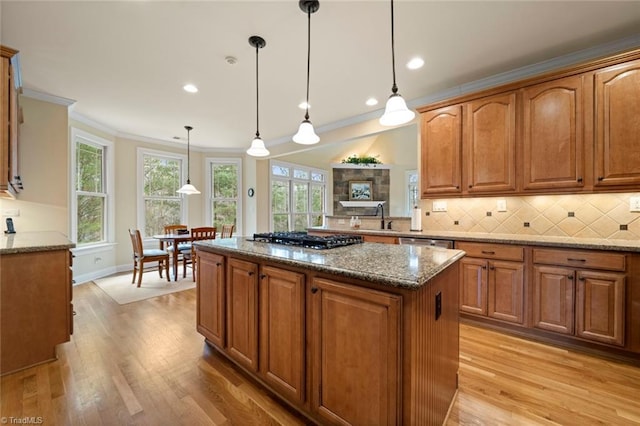 kitchen featuring tasteful backsplash, black gas cooktop, light wood-type flooring, stone counters, and a sink