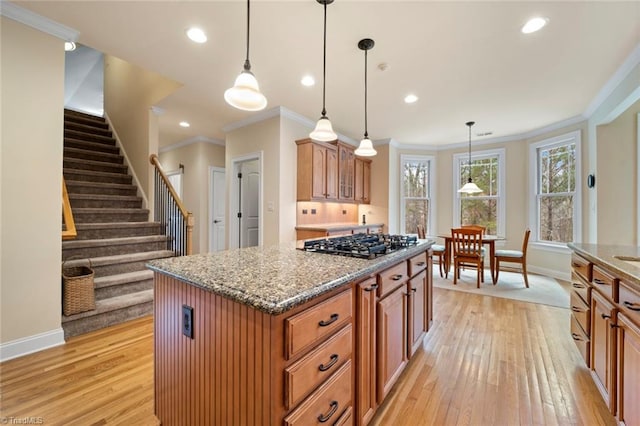 kitchen featuring stone counters, a kitchen island, stainless steel gas cooktop, decorative light fixtures, and light wood-type flooring