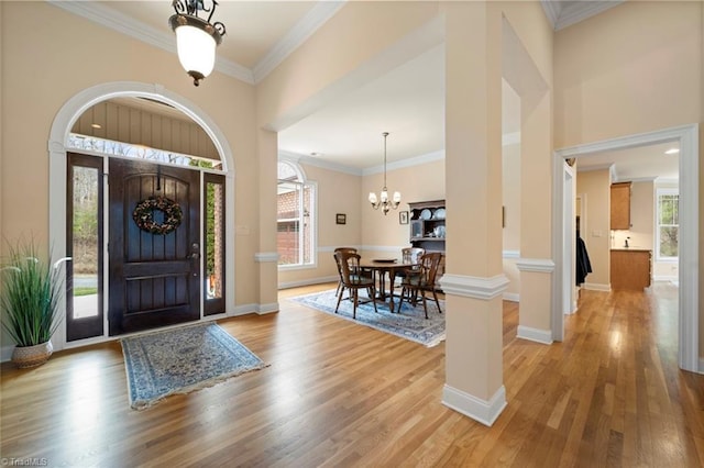 entrance foyer with baseboards, a chandelier, ornamental molding, a towering ceiling, and light wood-style floors