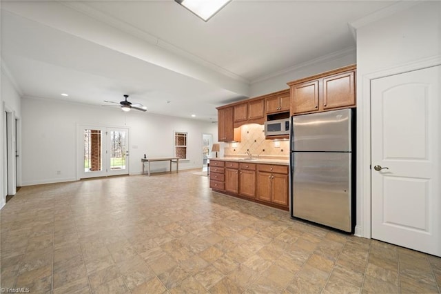 kitchen featuring white microwave, backsplash, baseboards, freestanding refrigerator, and brown cabinetry