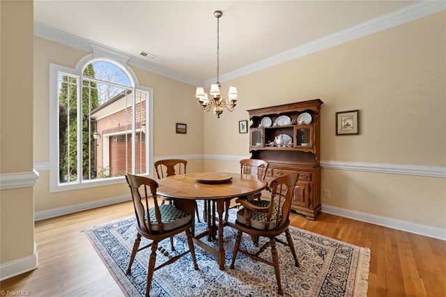 dining area with light wood finished floors, an inviting chandelier, baseboards, and ornamental molding