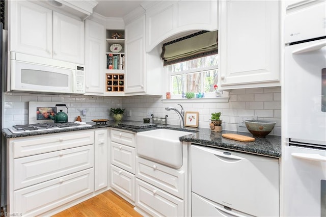 kitchen with white appliances, dark stone counters, white cabinets, tasteful backsplash, and a sink