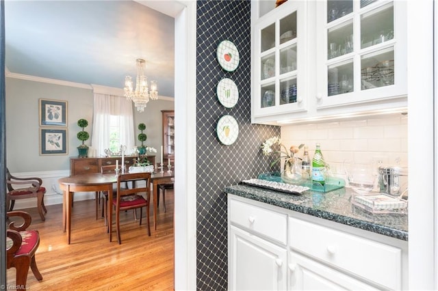 bar with hanging light fixtures, light wood finished floors, a chandelier, backsplash, and ornamental molding