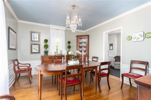 dining room with an inviting chandelier, ornamental molding, light wood finished floors, and wainscoting