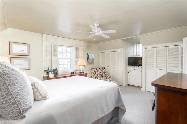 bedroom with vaulted ceiling, ceiling fan, two closets, and light colored carpet