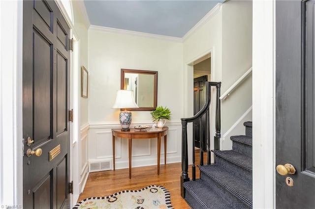 entrance foyer with light wood finished floors, a wainscoted wall, visible vents, ornamental molding, and stairway