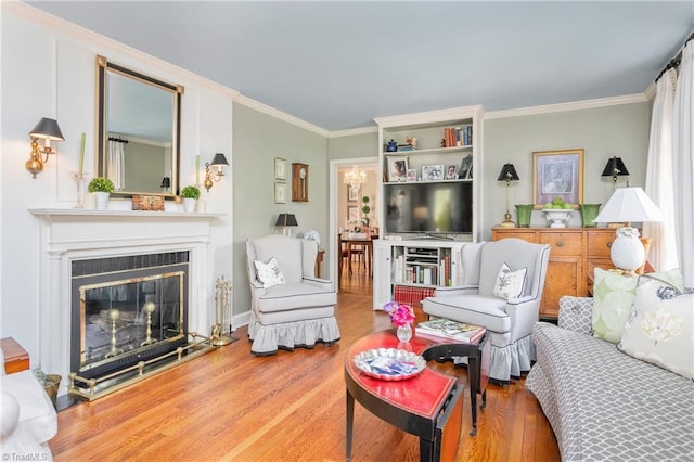 living area with crown molding, a glass covered fireplace, wood finished floors, and a chandelier