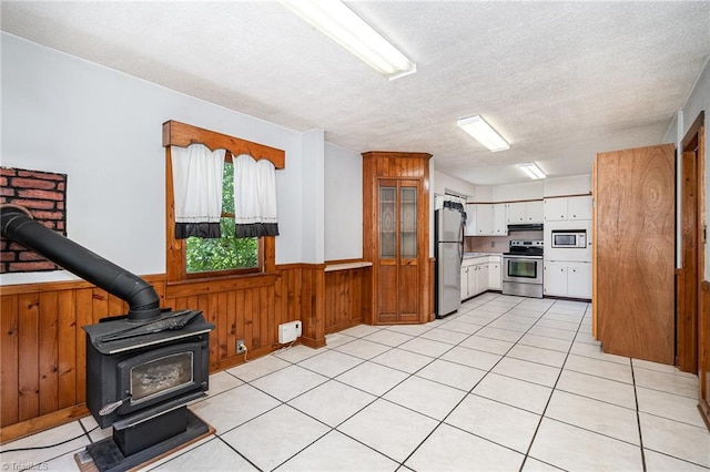 3753 Konnoak Dr SW, Winston-Salem, NC 27127 - kitchen featuring appliances with stainless steel finishes, a wood stove, wainscoting, a textured ceiling, and wooden walls