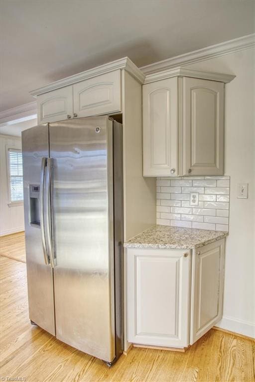 kitchen with light stone countertops, tasteful backsplash, stainless steel refrigerator with ice dispenser, crown molding, and light hardwood / wood-style floors