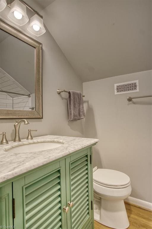 bathroom featuring vanity, wood-type flooring, lofted ceiling, and toilet