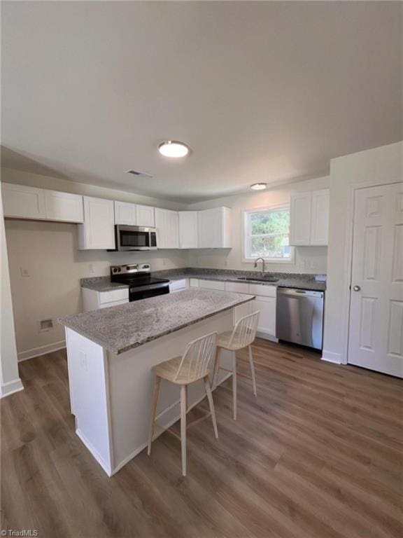 1609 Hardie St, Greensboro, NC 27403 - kitchen featuring stainless steel appliances, a kitchen island, dark wood-style floors, white cabinets, and a breakfast bar