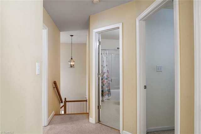 hallway featuring an upstairs landing, light colored carpet, and baseboards