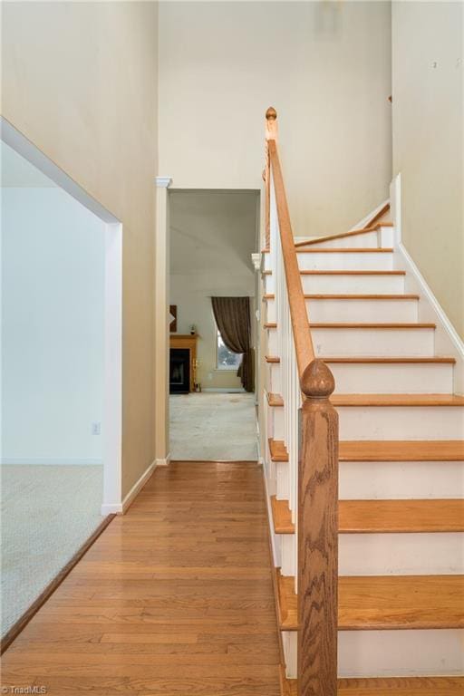 stairs with a fireplace, a high ceiling, baseboards, and wood finished floors